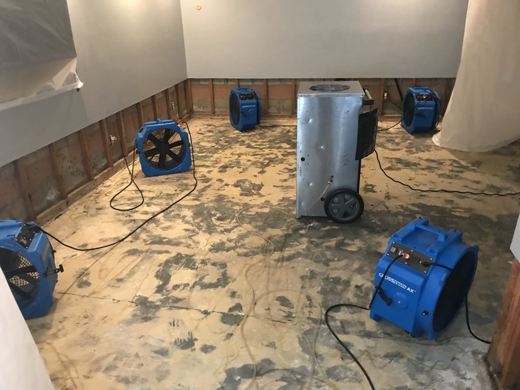Professional water damage restoration setup with multiple air movers and dehumidifier in a room with flood cuts